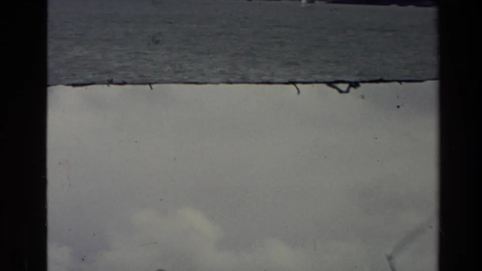 1981 New Zealand 8mm frame with a subdued water view, pale clouds, film grain, and worn frame edges.