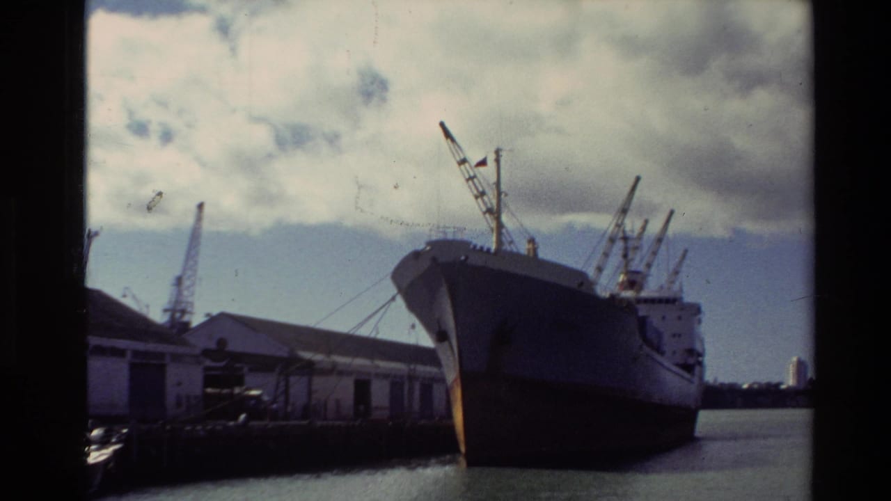 1981 New Zealand 8mm frame showing a large cargo ship at a dock with sheds, cranes, water, and cloudy sky.