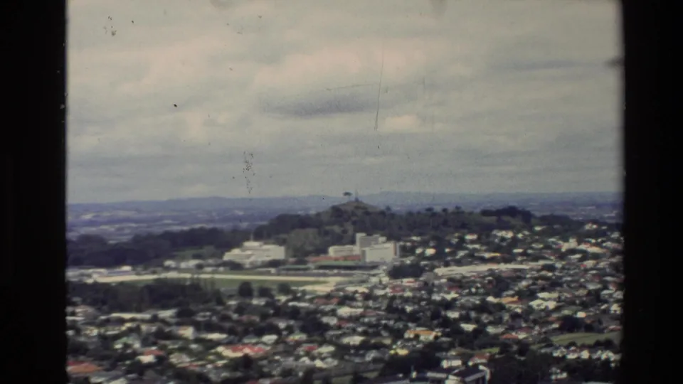 Wide 1981 New Zealand city view from an elevated vantage point, showing suburbs, roads, hills, and cloudy sky.