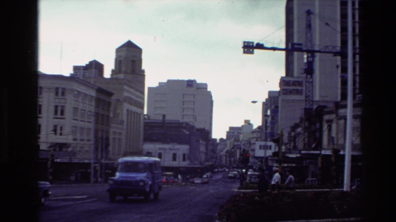 1981 New Zealand home-movie frame showing a city street intersection with traffic, pedestrians, older buildings, and visible theatre signage.