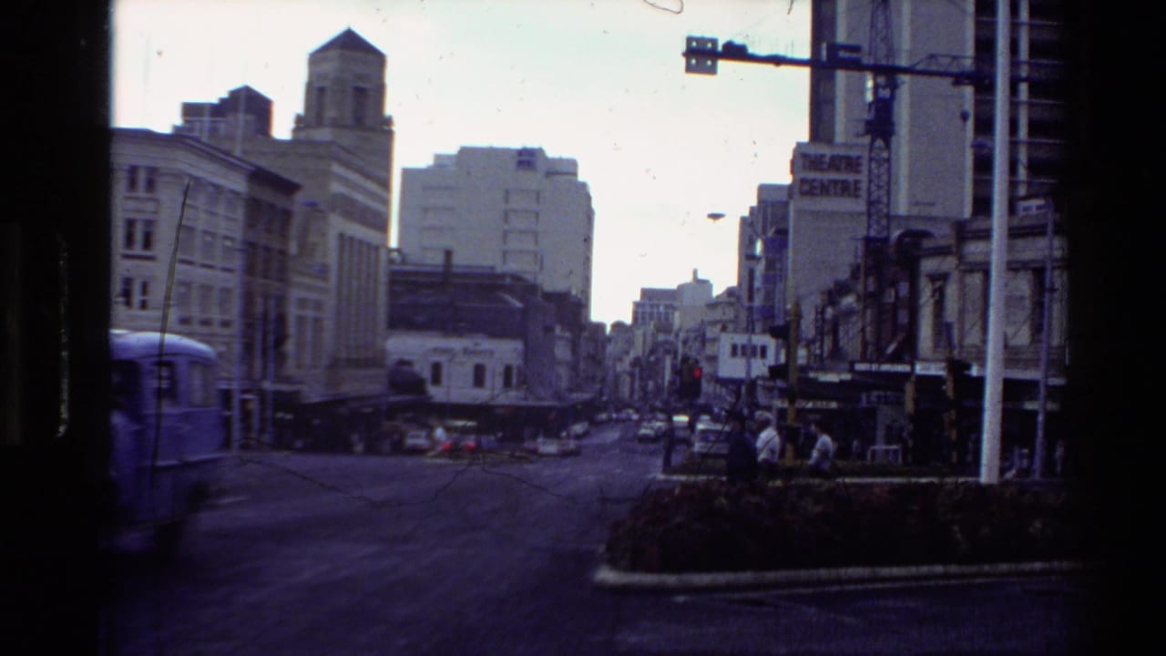 City street view with a blue van, theatre sign, buildings, and traffic lanes.