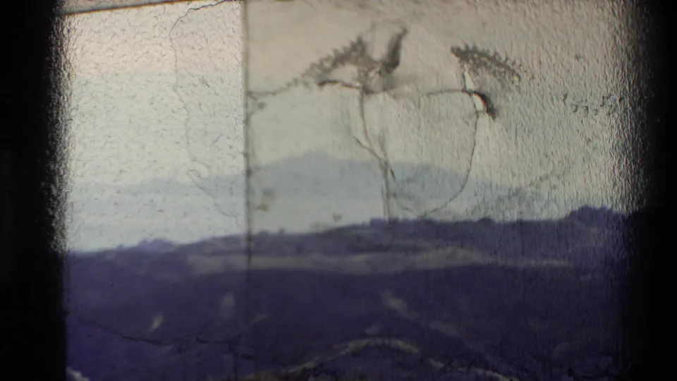 1981 New Zealand 8mm view of shadowed hills, pale water, and distant land through a worn film frame.