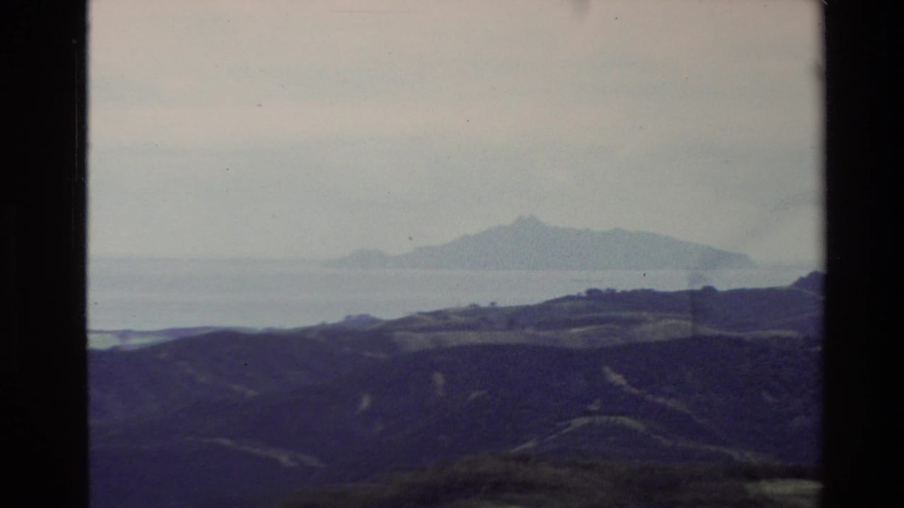 Coastal hills and a distant island or mountain across pale water under cloud.