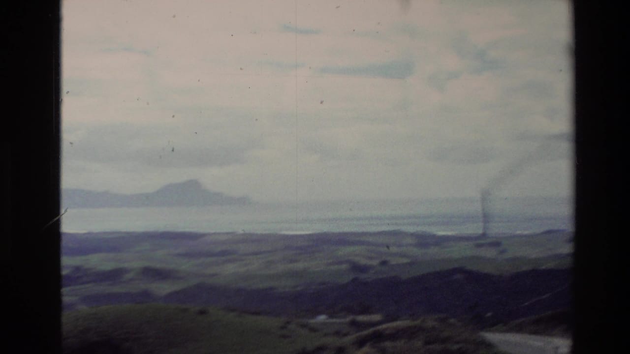 1981 New Zealand home-movie frame with green hills in the foreground, water beyond, distant island shapes, and visible 8mm frame marks.