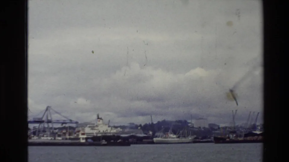 1981 New Zealand 8mm frame showing boats, a commercial vessel, cranes, and shoreline activity across the water.