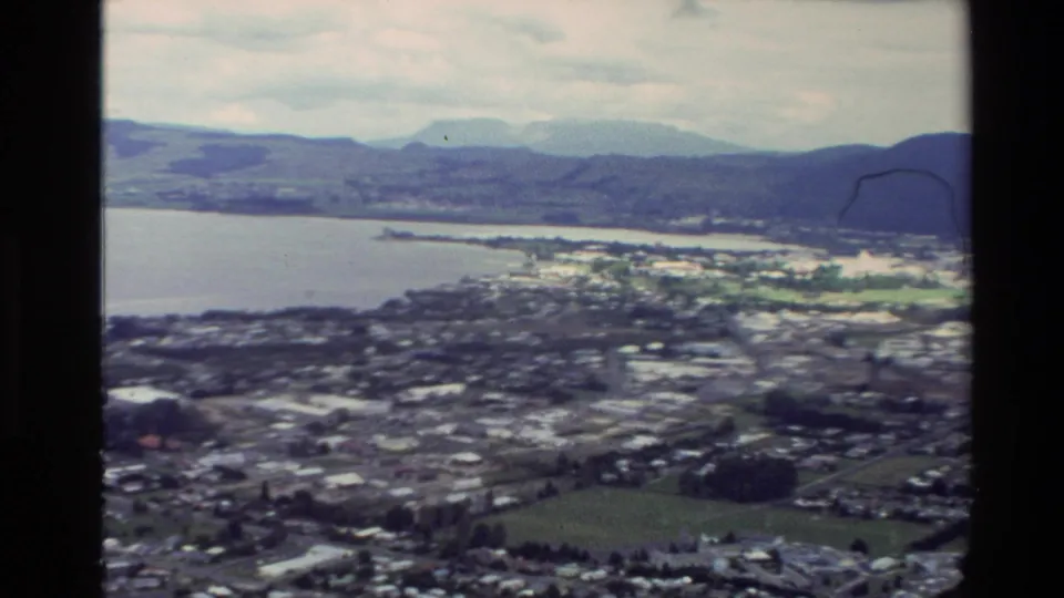 Elevated 1981 New Zealand home-movie view over a coastal town, waterfront, bay, and surrounding hills.