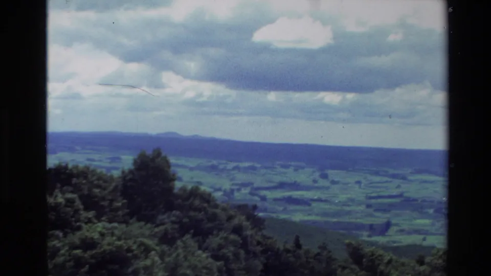 1981 New Zealand 8mm frame showing a panoramic rural view with trees, fields, distant hills, and low clouds.