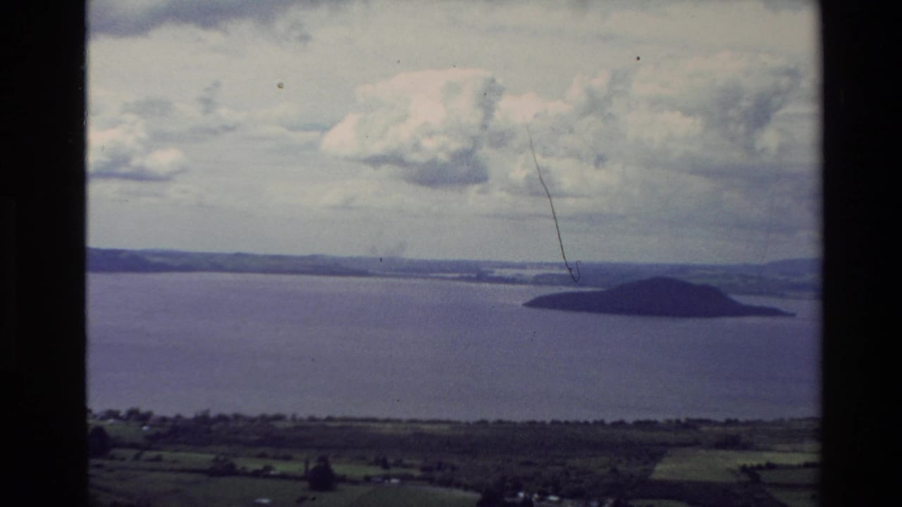 Wide coastal view with a dark island to the right, open water, distant shoreline, and heavy clouds.