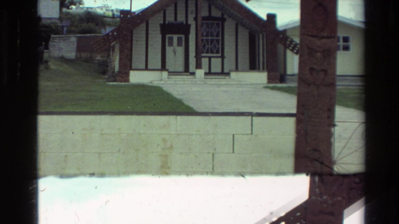 Similar view of the gabled meeting-house exterior with carved post and wall in front.
