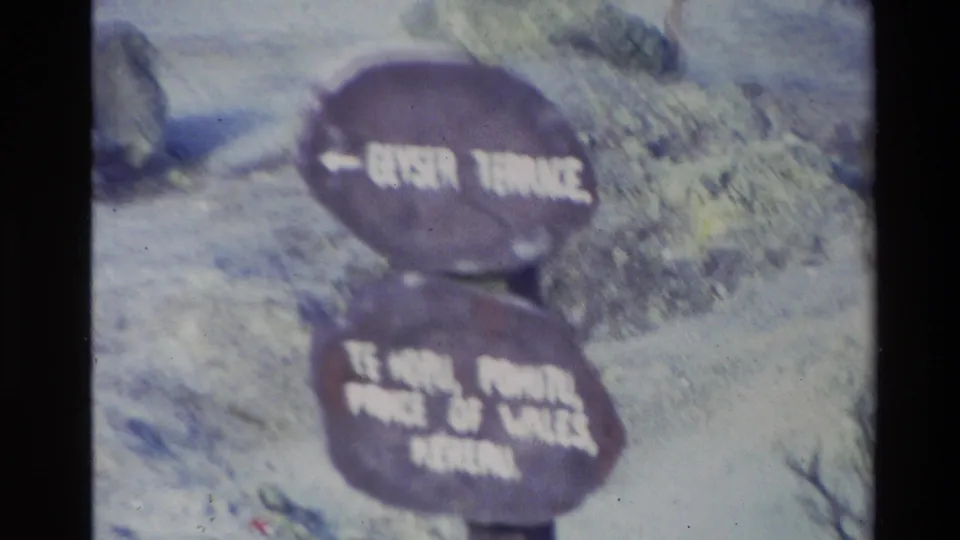 1981 New Zealand home-movie frame showing a weathered directional sign for Geyser Terrace and named geothermal features in rough terrain.