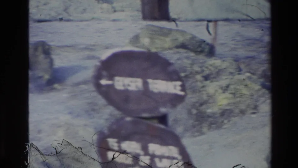 Soft 8mm frame of the wooden geyser-area sign, with lettering partly obscured by blur and frame-edge damage.