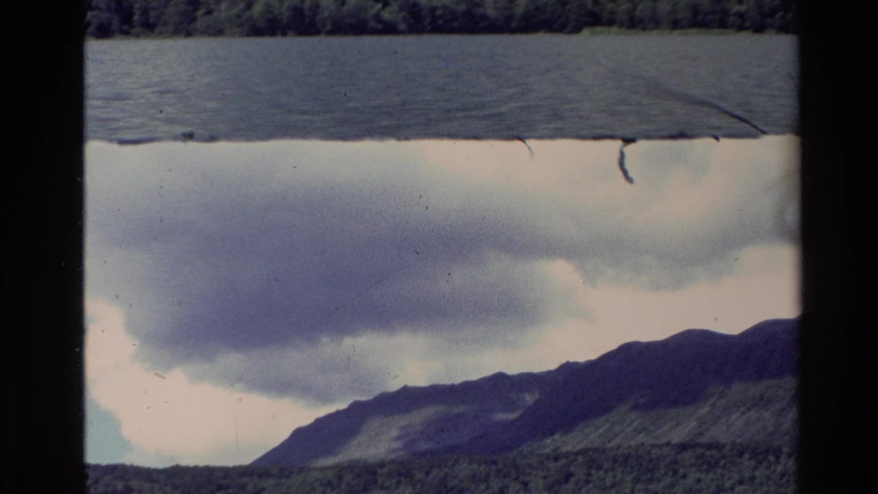Partly flipped film frame with lake, clouds, forest, and mountain ridge.