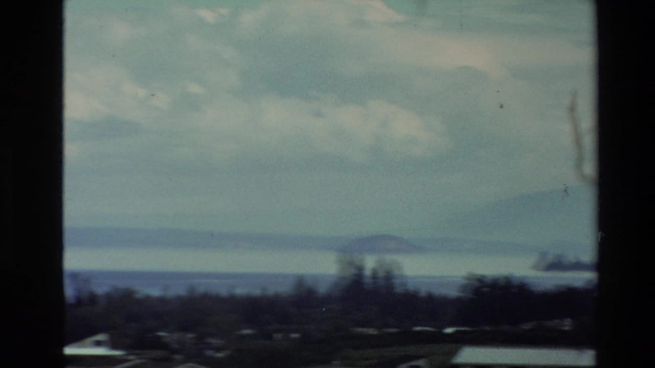 1981 New Zealand 8mm view of coastal water, low islands, trees, and cloudy sky with visible film-frame borders.