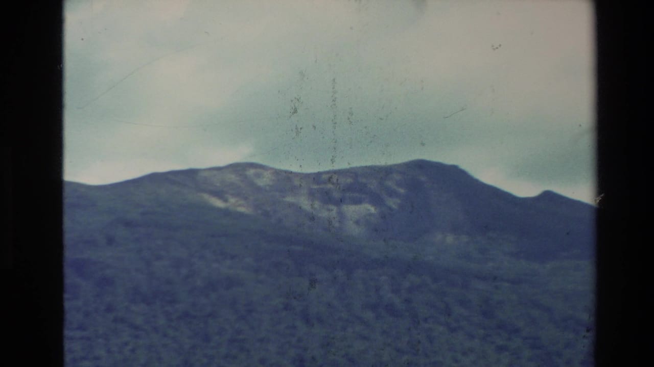 New Zealand 1981 home-movie frame showing layered mountain ridges beneath an overcast sky with visible 8mm grain and gate edge.