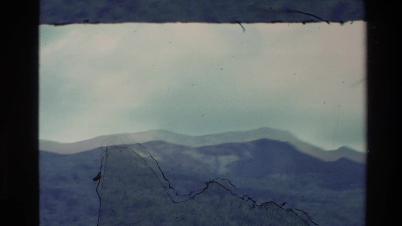 Distant mountain ridges with visible scratches and dark film borders.