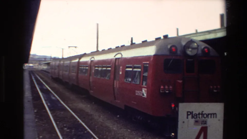 New Zealand 1981 rail-station frame showing a red passenger train at Platform 4, parallel tracks, canopy structure, and dark film borders.