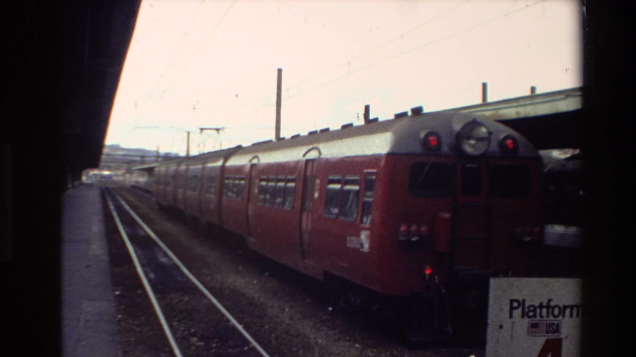 1981 New Zealand 8mm frame showing a red passenger train at a station platform, seen through dark train-window edges.