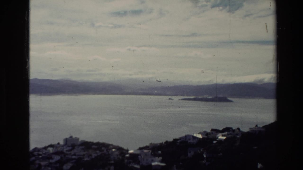 Wide coastal view with ocean, island, distant hills, clouds, and dark hillside foreground.