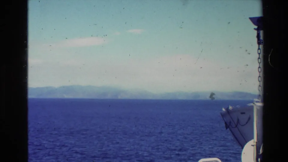 1981 New Zealand 8mm frame looking across blue ocean toward hazy mountains, with a partial boat structure or railing visible at right.