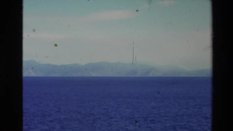 1981 New Zealand 8mm seascape with deep blue water, a pale sky, and hazy mountain landforms stretching across the horizon.