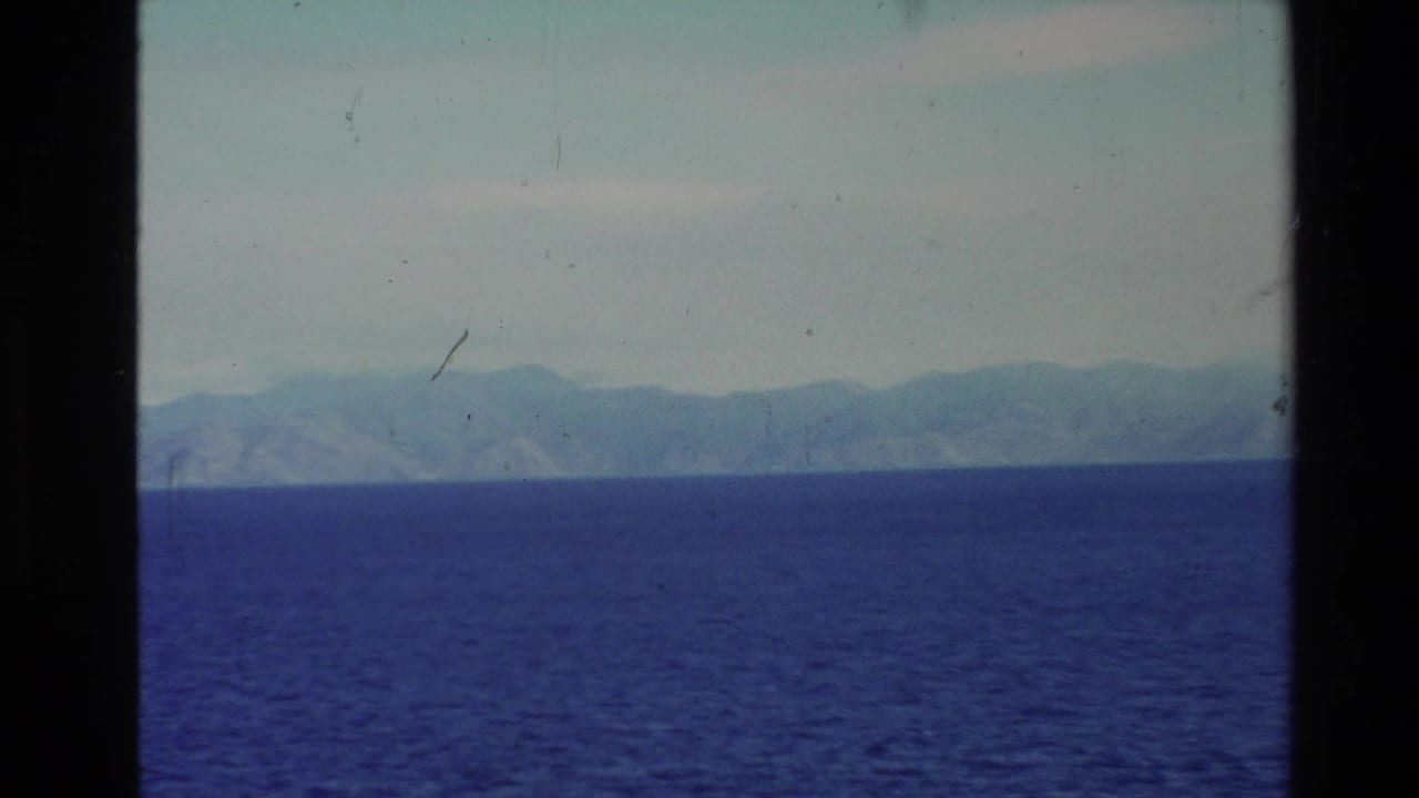 1981 New Zealand 8mm frame showing blue sea and a hazy mountainous coastline through dark vertical framing.