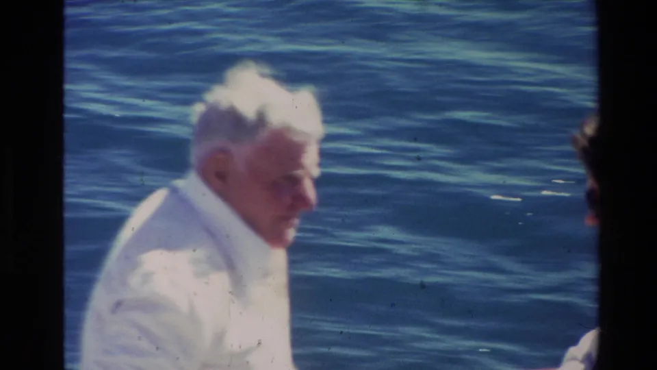 Soft 1981 New Zealand 8mm frame of an older white-haired man on or near a boat, with blue water behind him.