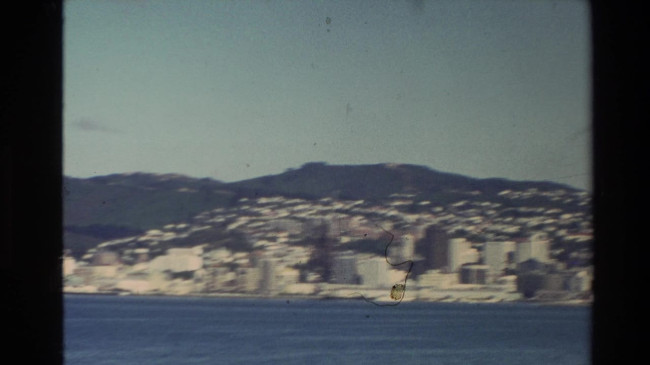 Coastal city across blue water with hills behind it and dark film borders.