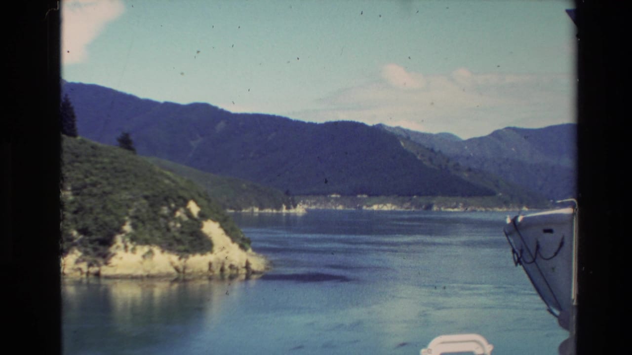 Calm lake with green hillside, distant mountains, and part of a boat bow.