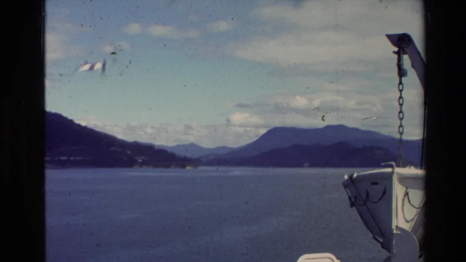 1981 8mm boat perspective across a broad lake, with dark shoreline hills, distant mountains, and white bow hardware visible.