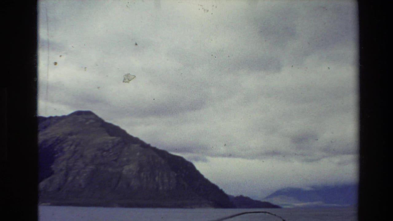 Steep mountain beside a lake under a heavy overcast sky.