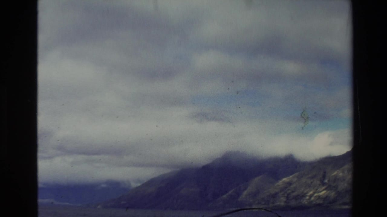 1981 New Zealand 8mm frame showing cloud-covered mountains and water, with soft exposure and visible film edges.