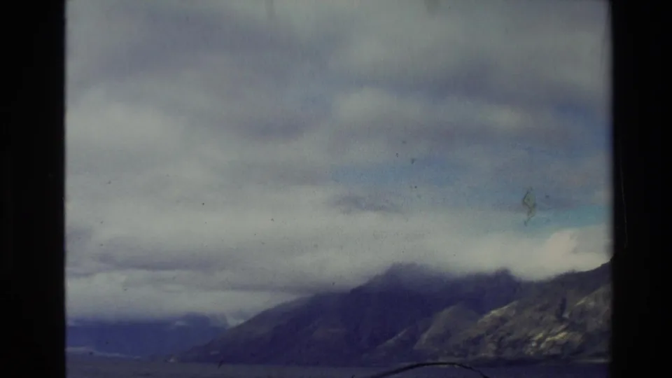 1981 New Zealand 8mm frame showing cloud-covered mountains and water, with soft exposure and visible film edges.