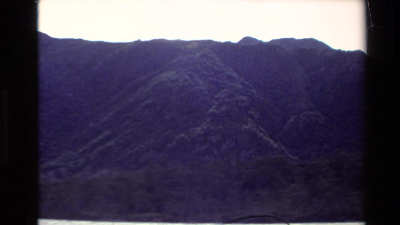 Steep mountain ridge fills the frame above a narrow strip of water.
