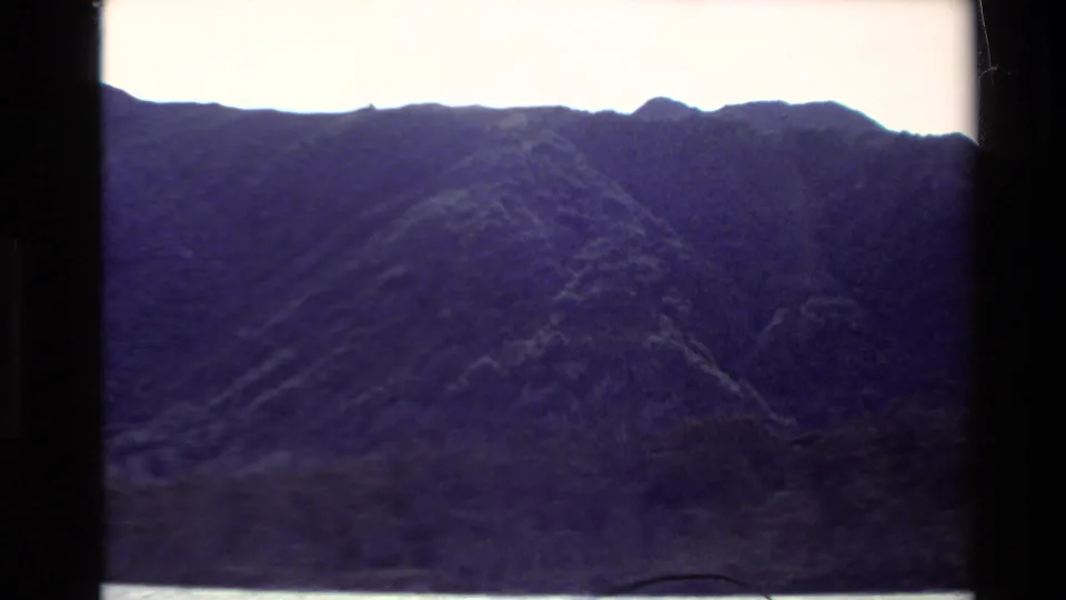 1981 New Zealand 8mm frame with a steep, dark mountain ridge above water, framed by visible scan borders.
