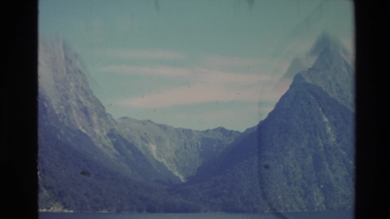 1981 New Zealand 8mm frame showing steep mountains and calm fjord water with soft blue-green film color.