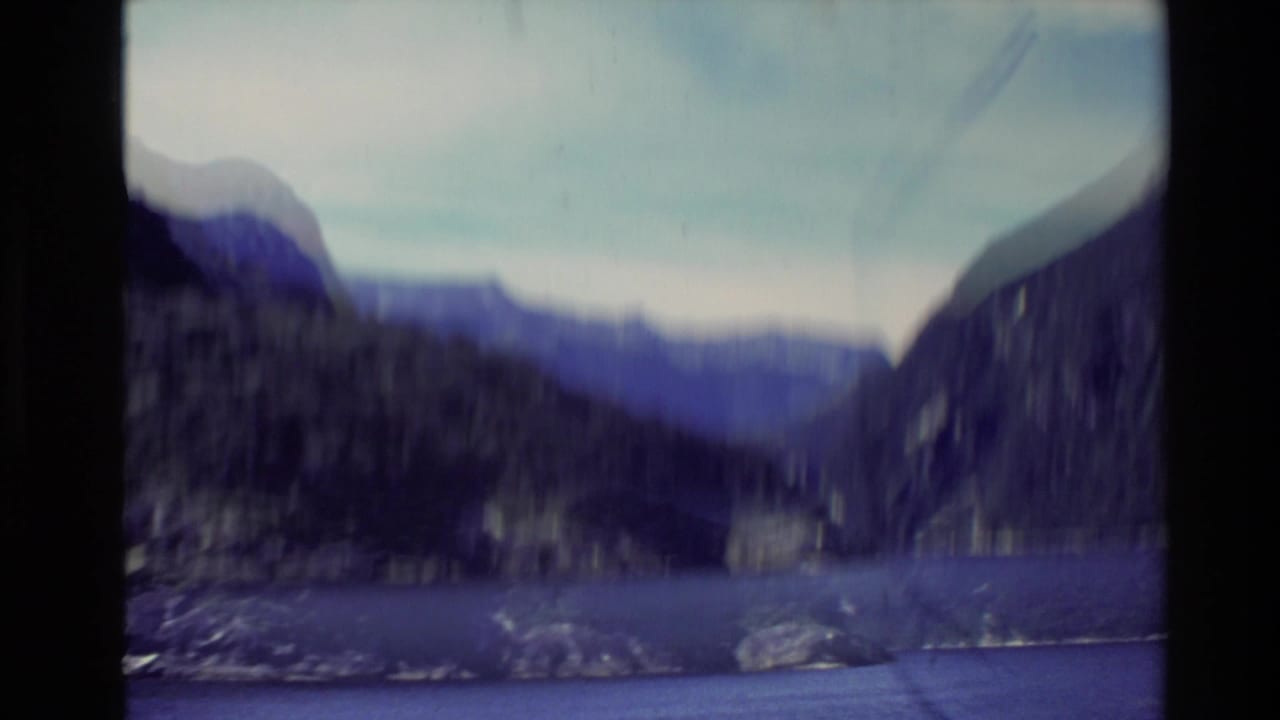 Soft handheld view of dark mountains, a valley, pale sky, and a bright streak across the frame.