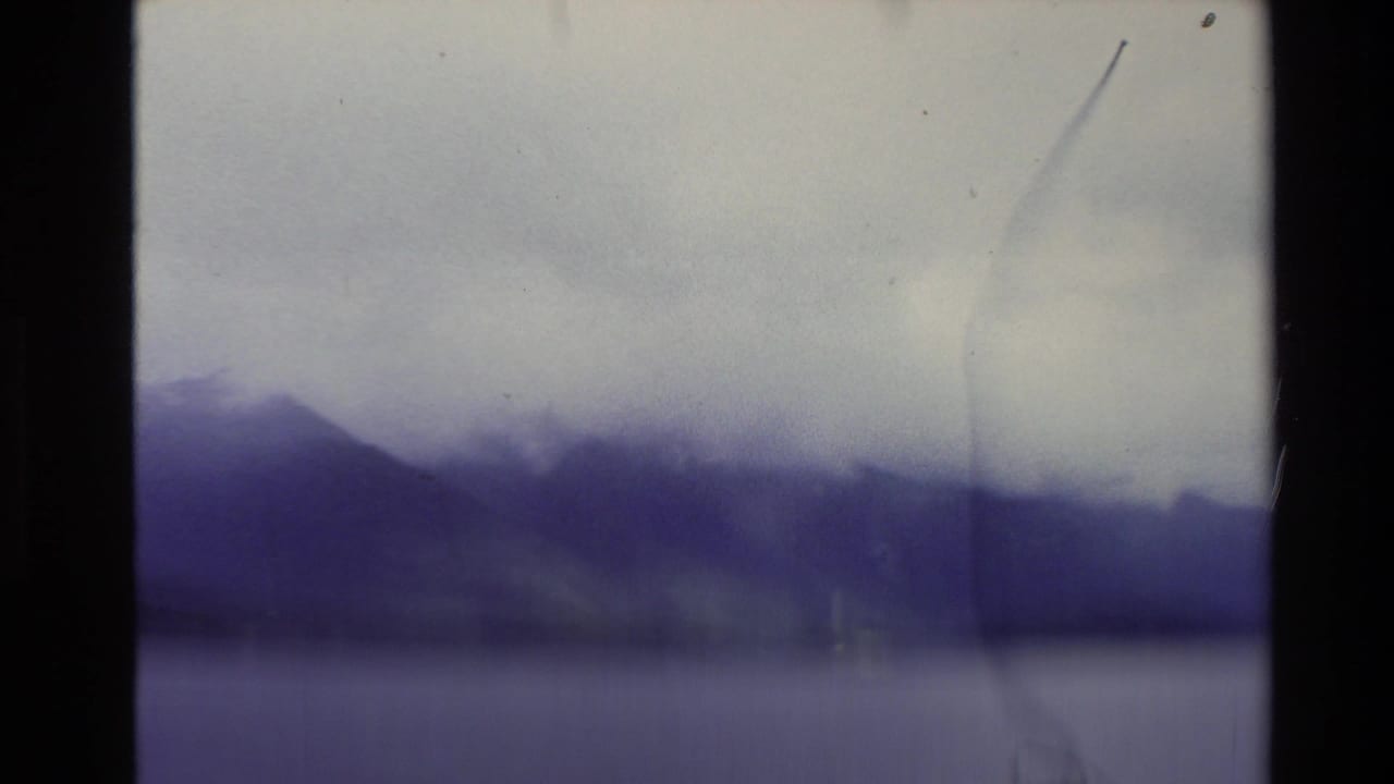 Clouded mountain ridge and water seen through soft purple-tinted film.