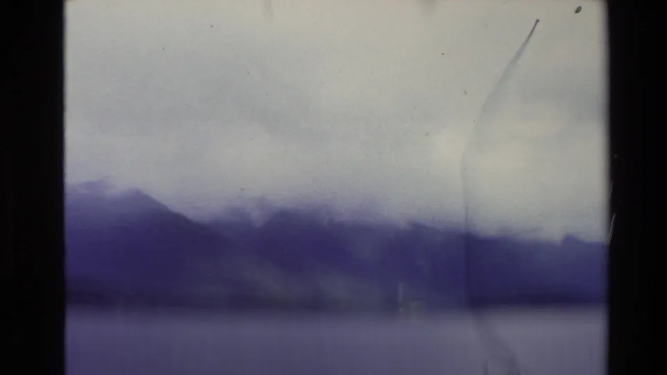 1981 New Zealand travel frame with a mountain ridge partly hidden by cloud above a smooth body of water.