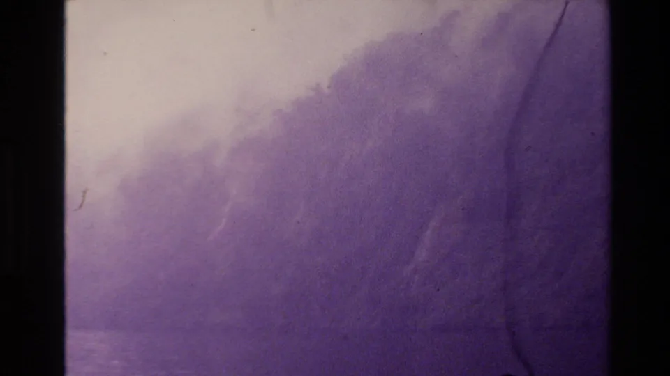 Faded 1981 New Zealand 8mm frame showing a distant wooded hillside through haze, with lavender cast and visible film wear.