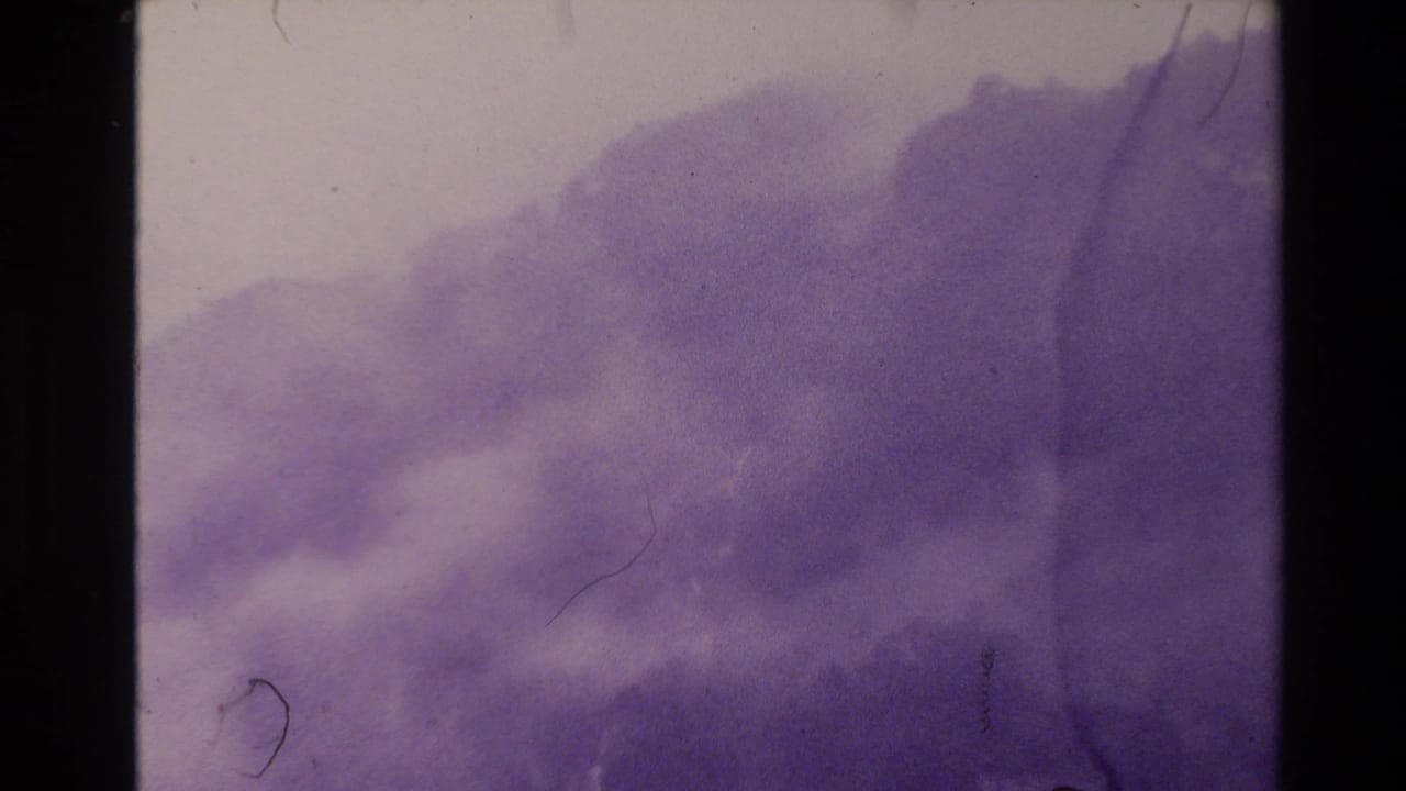 Foggy purple hillside and pale sky with black film borders and surface scratches.