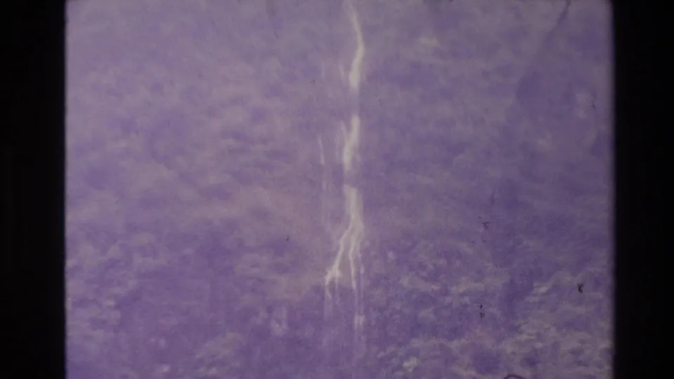 1981 New Zealand 8mm frame showing faint cascading water through purple color shift, grain, scratches, and dark frame borders.
