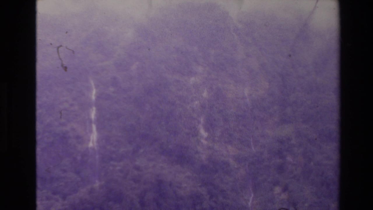 Soft purple landscape texture with thin pale waterfall lines and visible film scratches.