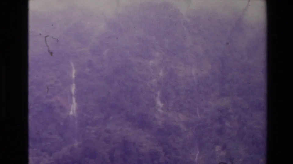 Purple-shifted 8mm frame from New Zealand with distant waterfall traces, grain, emulsion marks, and heavy scan texture.