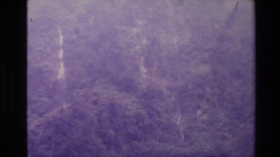 1981 New Zealand 8mm frame with multiple faint waterfall streaks, purple dye shift, scratches, grain, and dark frame borders.