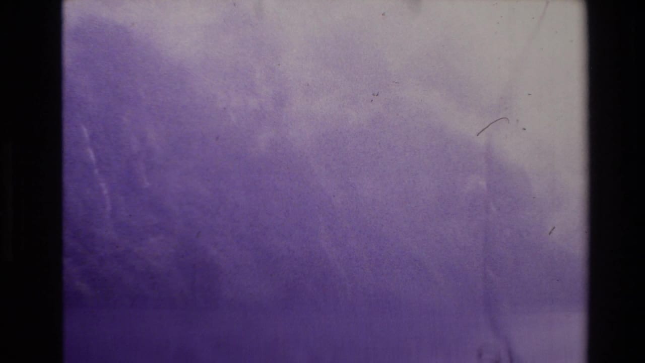 Soft 8mm frame from the New Zealand clip showing abstract purple lake or sky tones with scratches and uneven exposure.