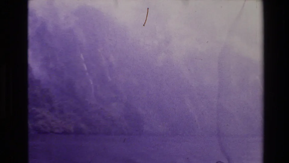 1981 New Zealand 8mm frame with a vague lake or mountain surface, purple color drift, scratches, and heavy softness.