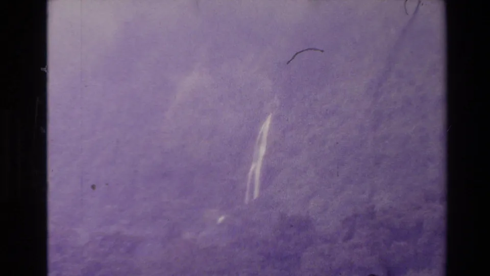 Soft 1981 New Zealand 8mm frame with indistinct lake or mountain forms, bright film streaks, scratches, and purple cast.
