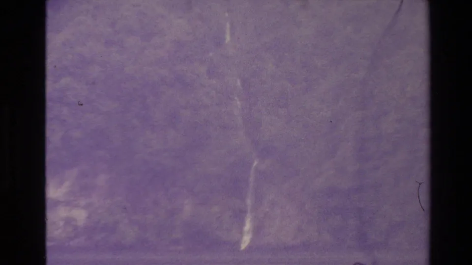 New Zealand 8mm frame from 1981 showing a faint waterfall among trees, with heavy purple aging, grain, and surface scratches.