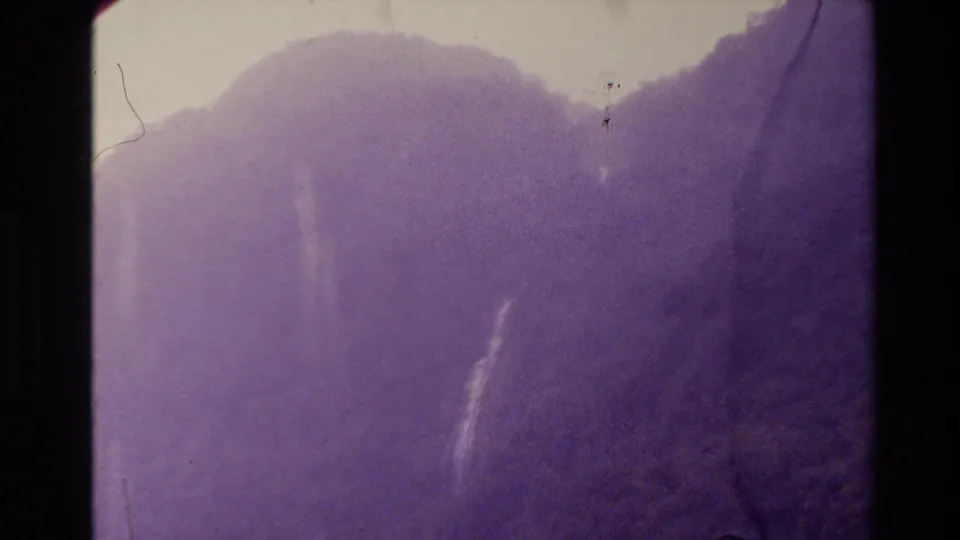 1981 New Zealand 8mm frame revealing a steep misty slope and faint distant waterfall through purple-tinted film wear.