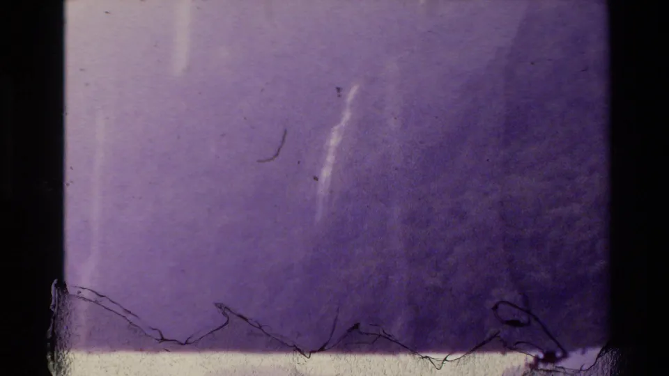 1981 New Zealand home-movie frame showing fog over a forested slope with a faint waterfall and visible 8mm wear.